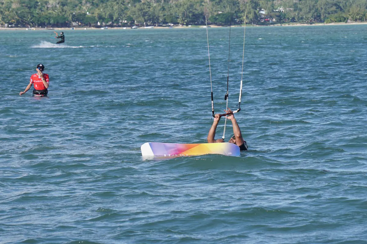 A kiter in the Le Morne lagoon holds the bar and picks up the board while the instructor watches nearby